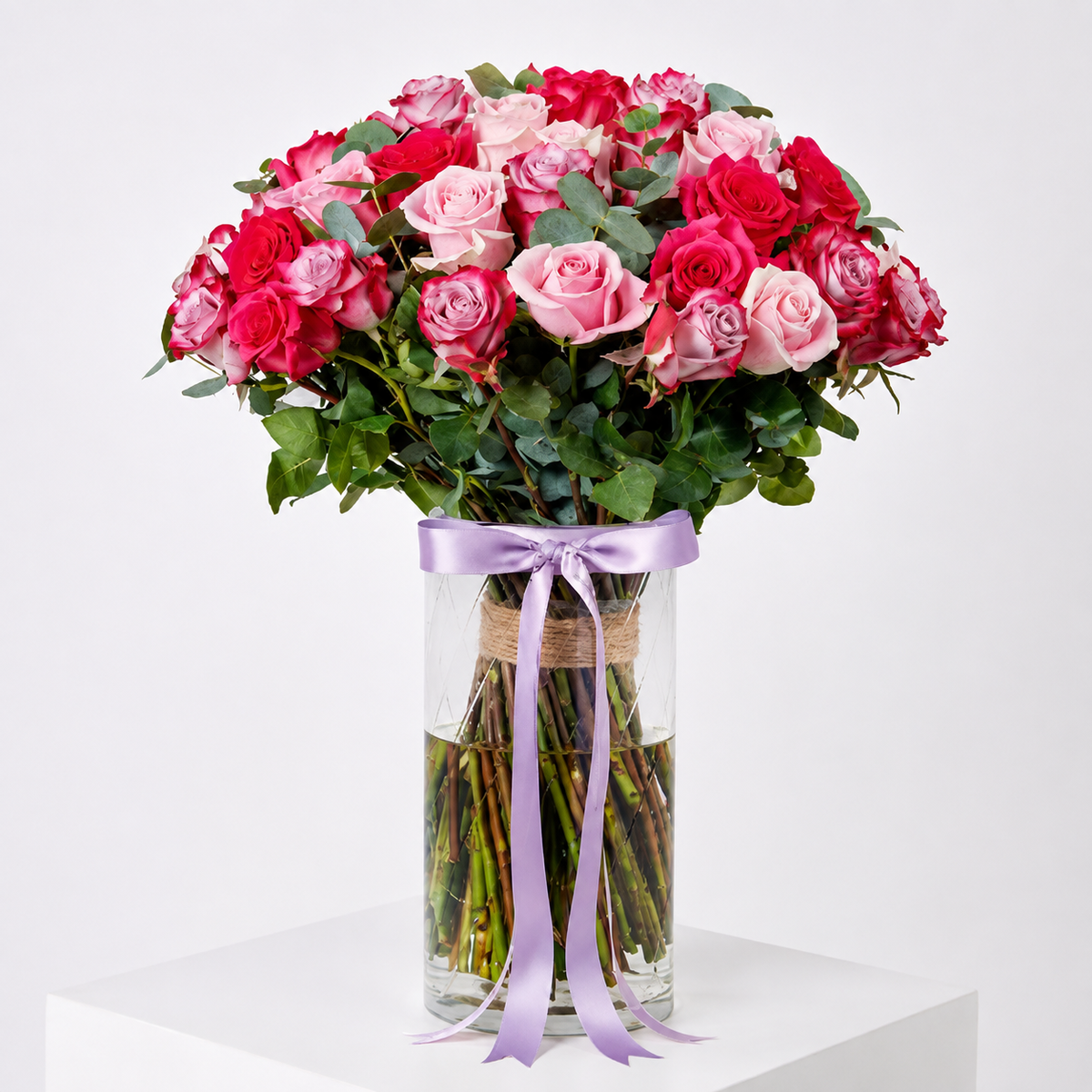 25 mixed red, pink and purple roses with greenery arranged in a glass vase