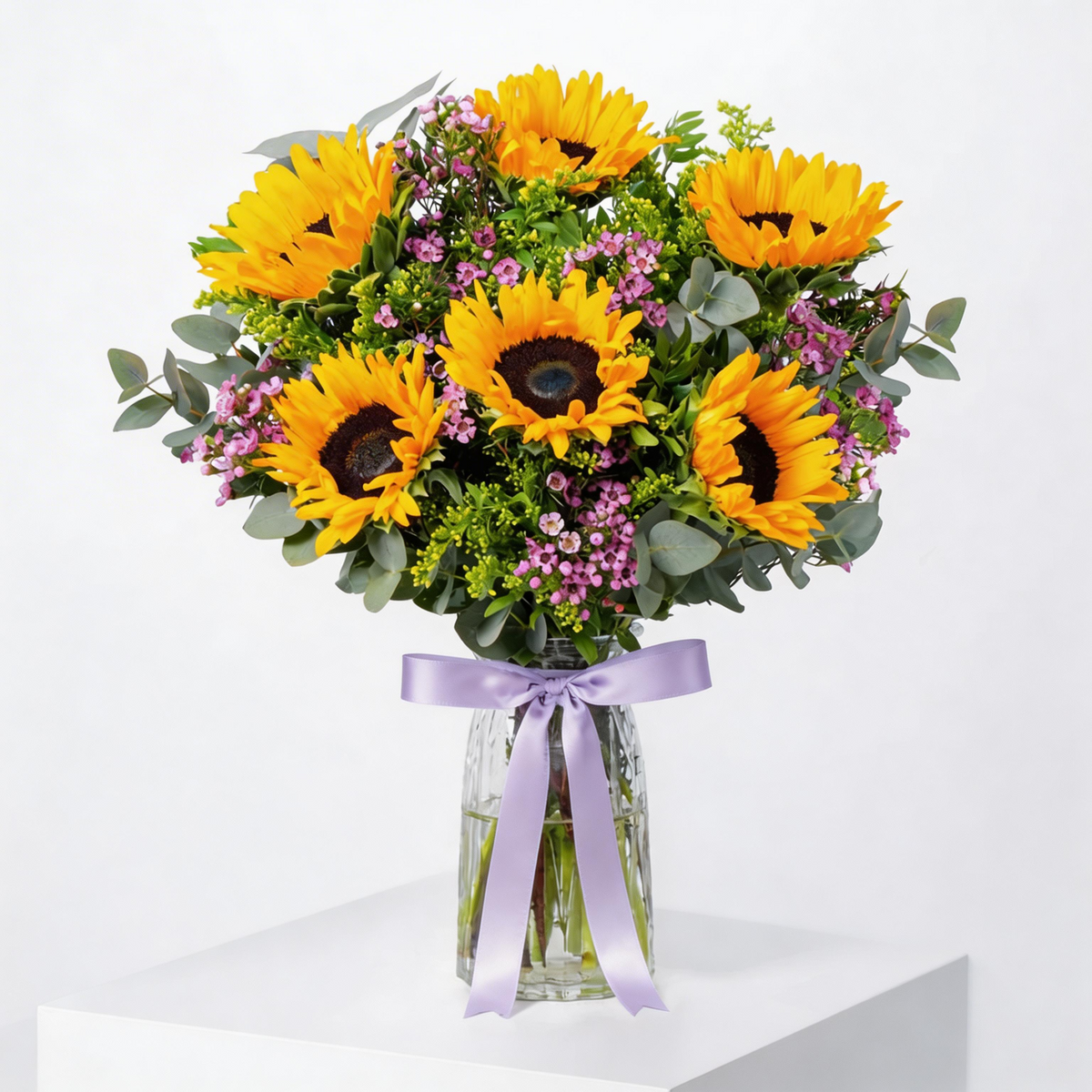 Sunflowers in a clear vase with a purple ribbon