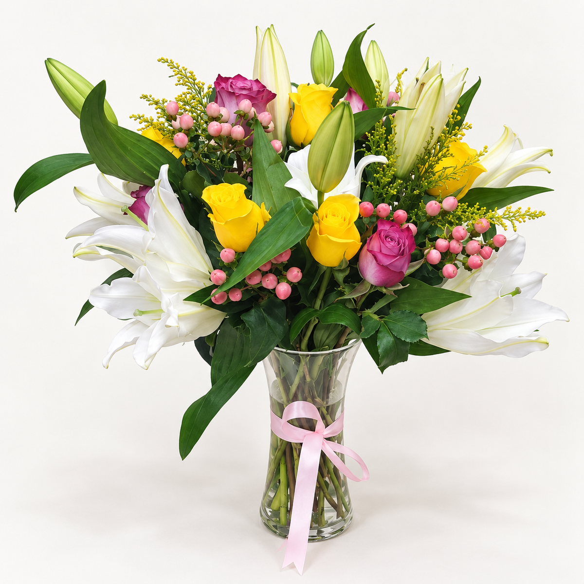 White lilies with purple and yellow roses, pink hypericum and greenery in a glass vase